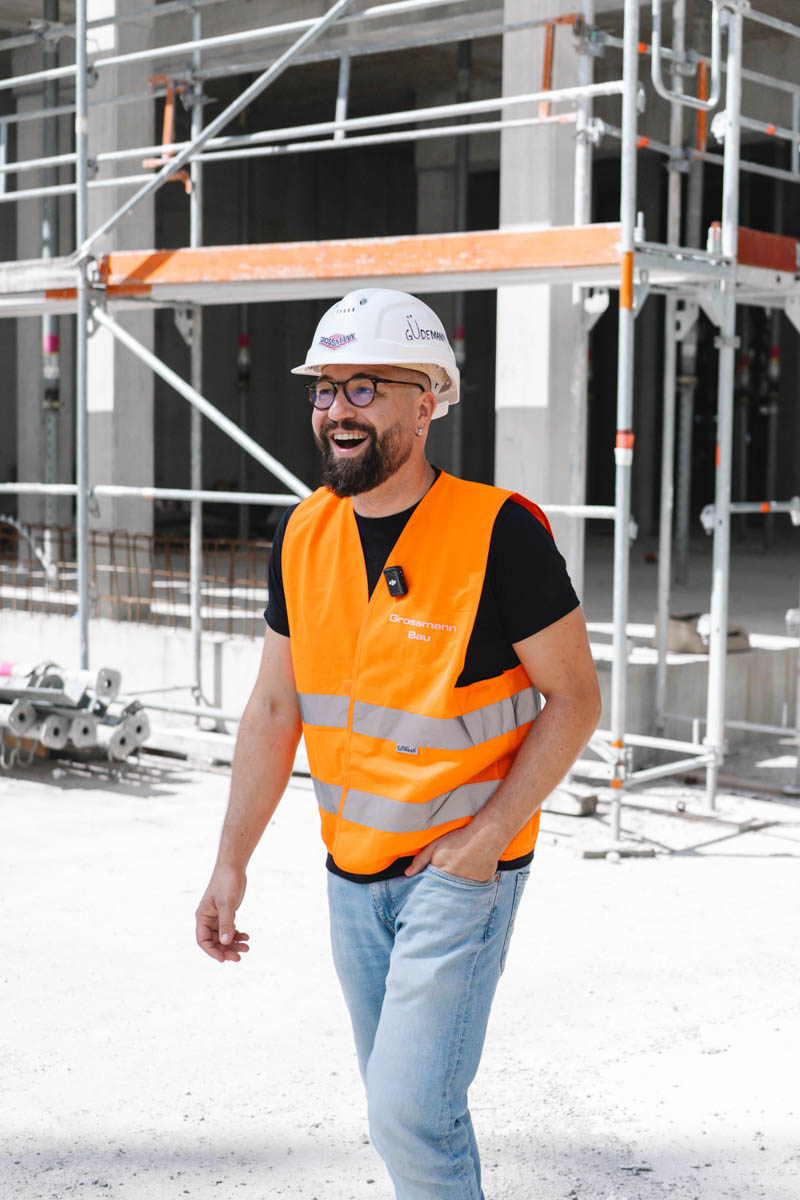 Mitarbeiter von Grossmann in Warnweste steht auf einer sonnigen Baustelle